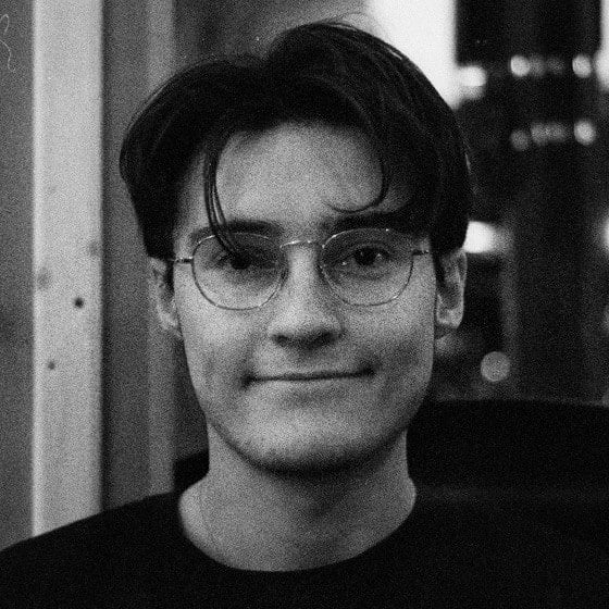 A black and white portrait of me: glasses, dark hair, half-smiling, in front of a workbench