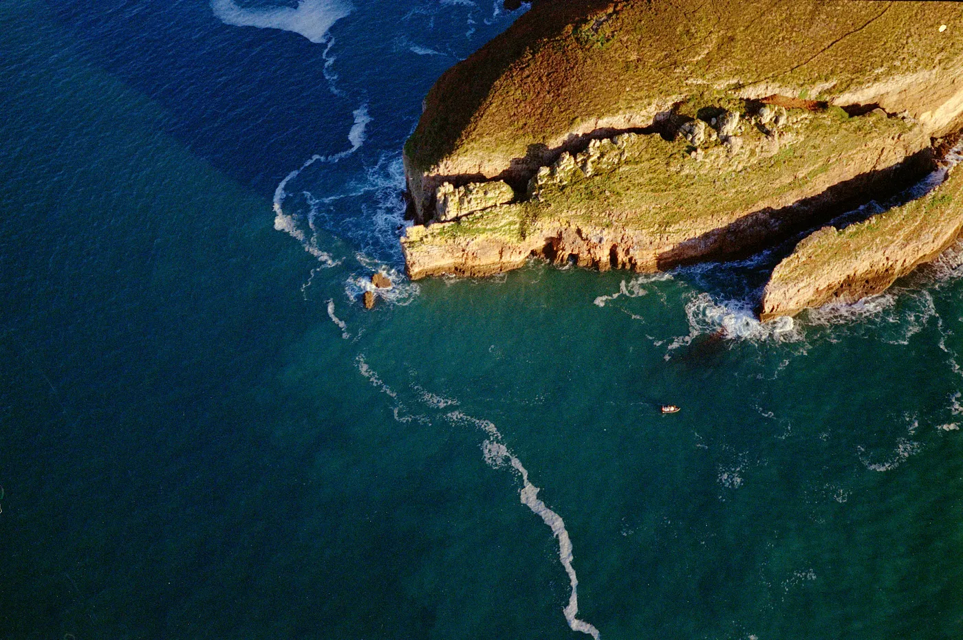 White cliffs meeting a blue sea, seen from the air, a line of foam along the shore.