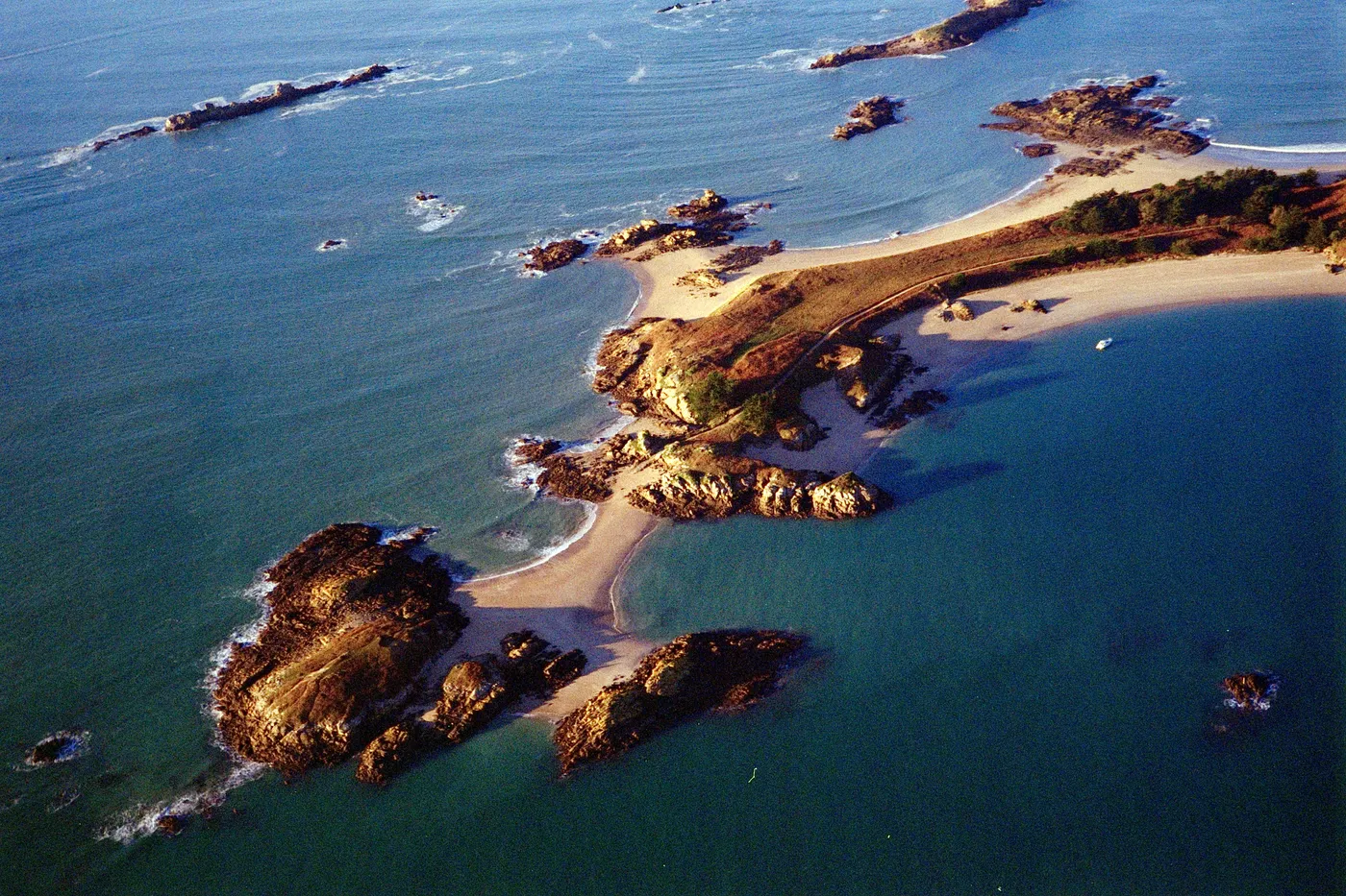 Rocky islets and a sandy spit seen from the air, in a turquoise sea at low tide.