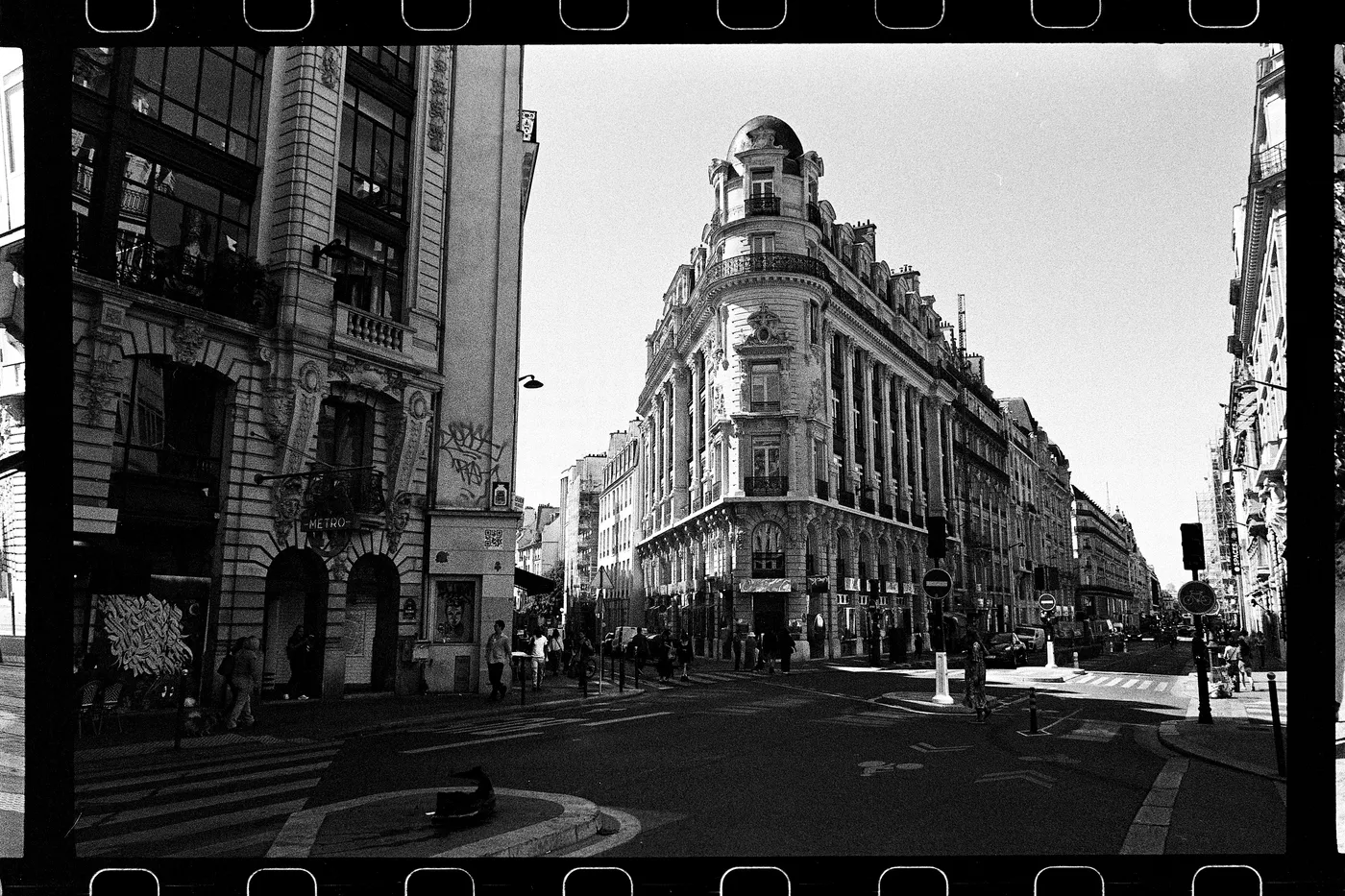 A Paris street corner in black and white, a Haussmann building with a domed roof, the film's sprocket holes showing along the edges.