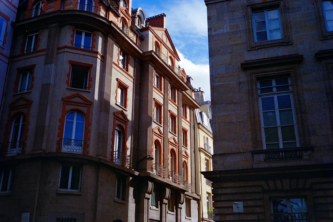 Haussmann facades in Paris, one sunlit and one in deep shadow, against a blue sky with a few clouds.